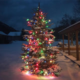 Outdoor Christmas tree with colored lights, surrounded by snow.